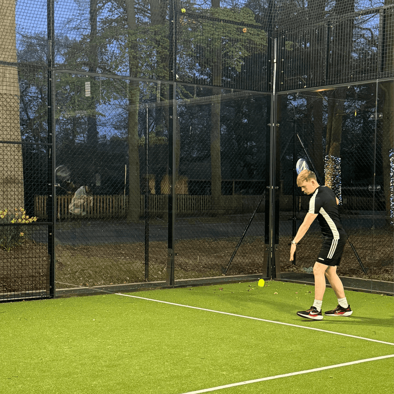 Man playing padel tennis on a green outside court.