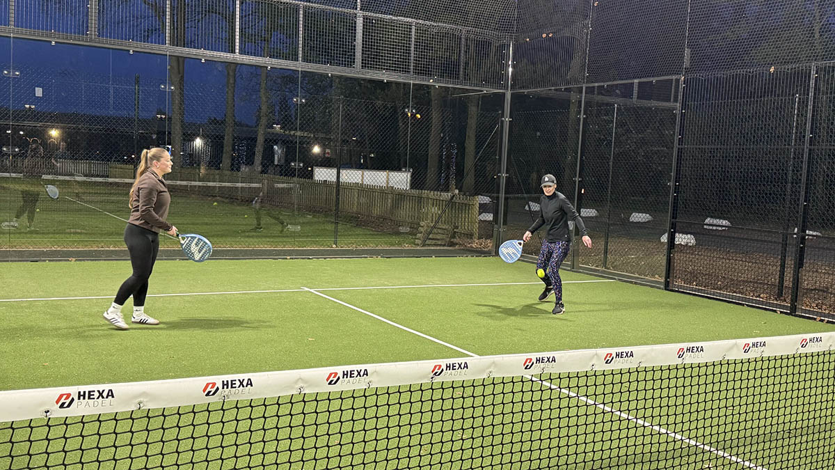 Two women playing padel tennis outside on a green court.