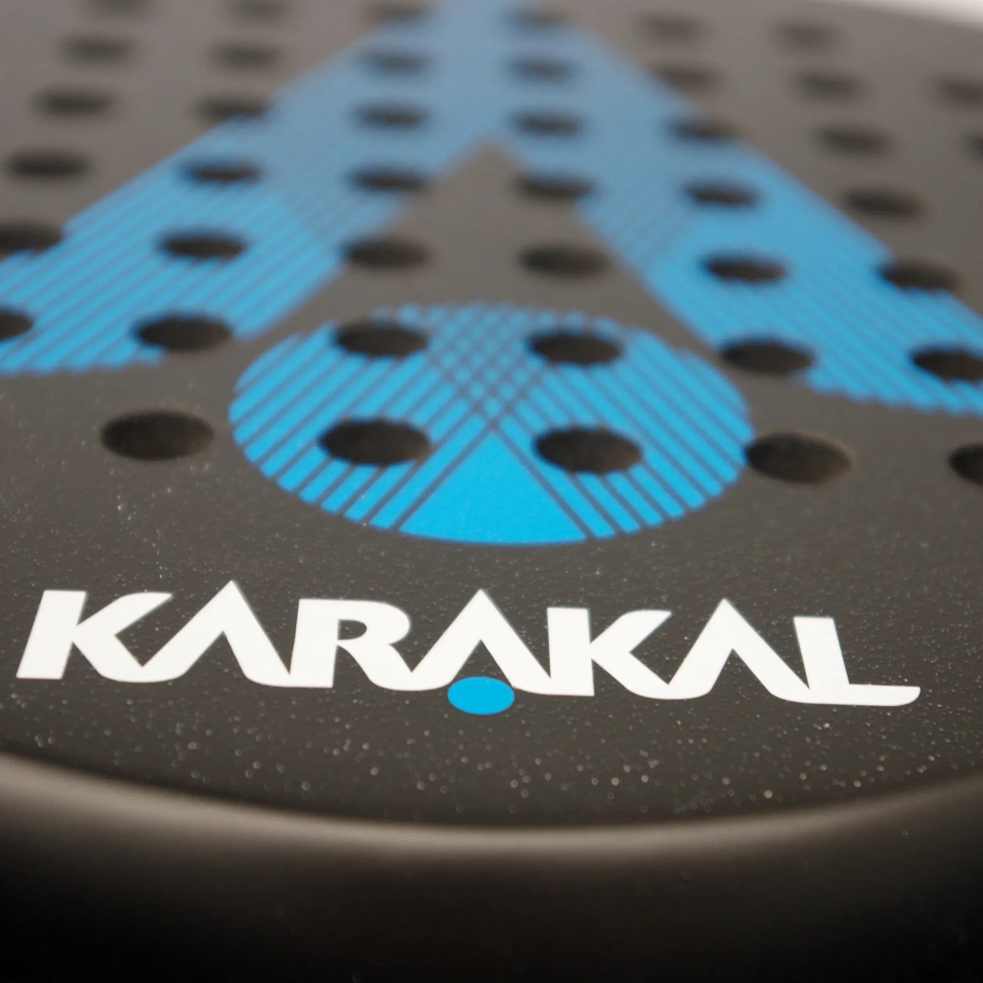 Close up of the face of a black and blue Karakal padel tennis racket on a white background.