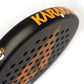 Close up of the top of a black and orange Karakal padel tennis racket on a white background.