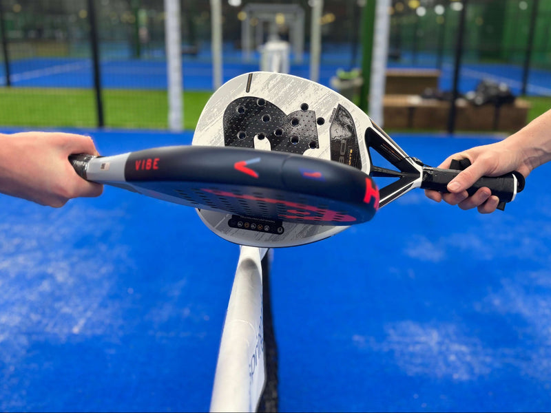 Two padel rackets touching on the net of a padel court.