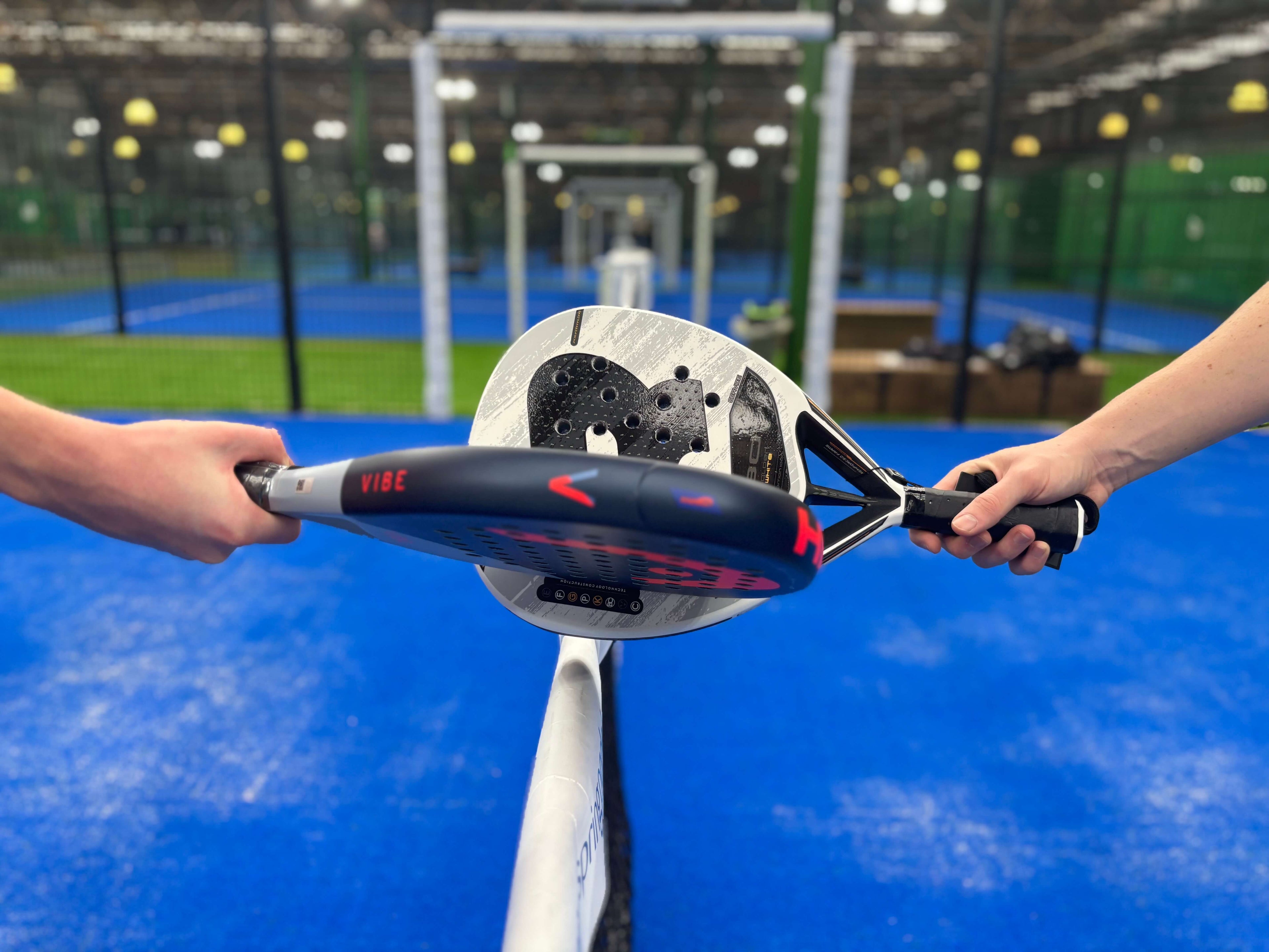 Two padel rackets touching on the net of a padel court.