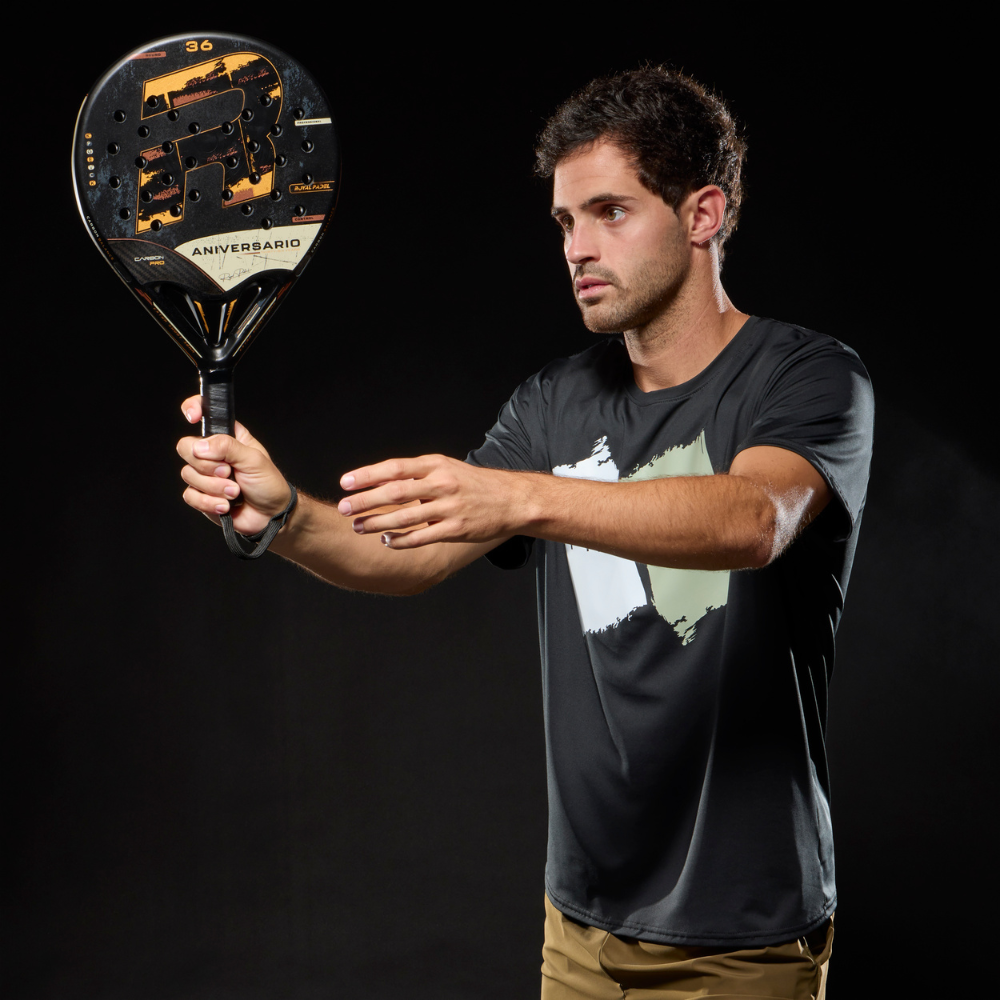 A man holding a black and gold Royal Padel Anniversario padel racket on a black background.