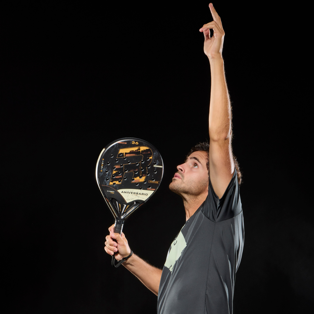 A man holding a black and gold Royal Padel Anniversario padel racket on a black background.