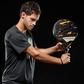 A man holding a black and gold Royal Padel Anniversario padel racket on a black background.