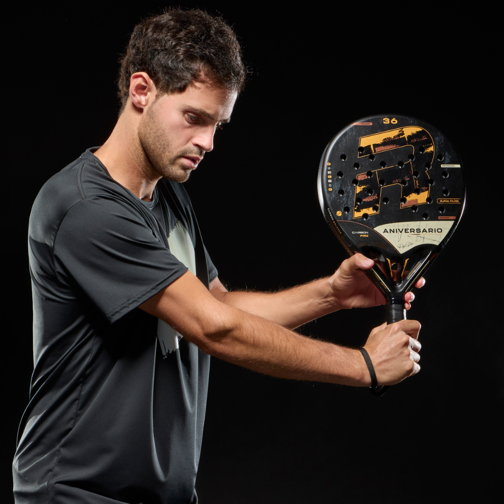 A man holding a black and gold Royal Padel Anniversario padel racket on a black background.