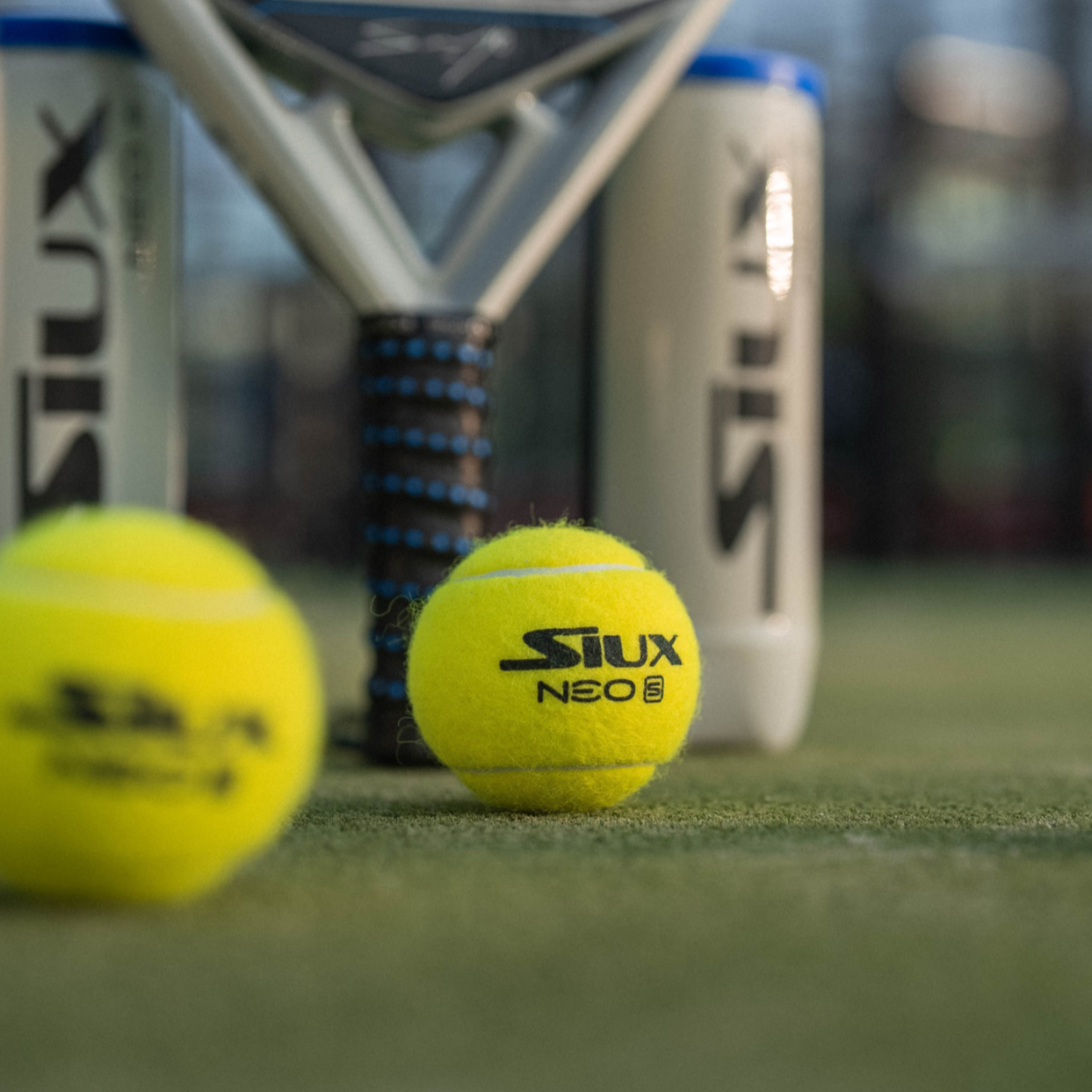 Two padel balls and a racket with 'Siux' branding on a padel court.