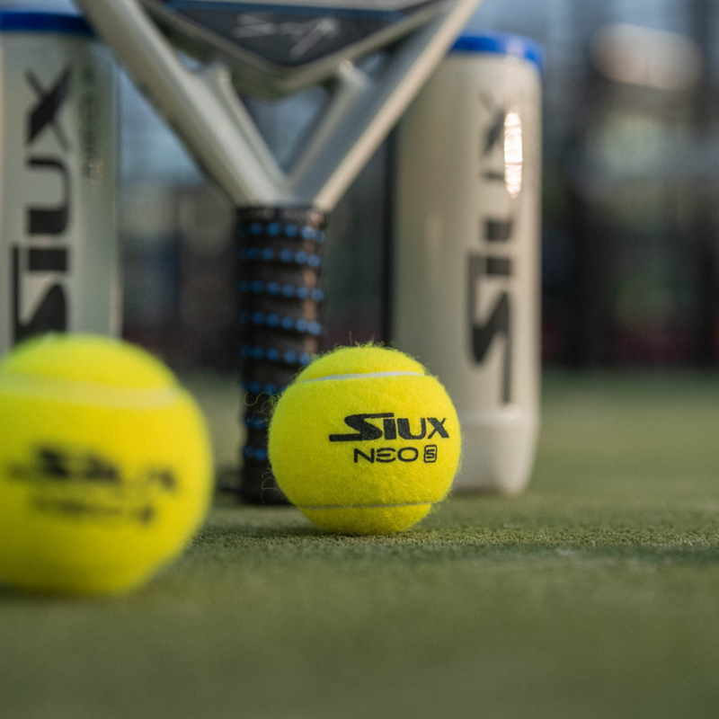 Two padel balls and a racket with 'Siux' branding on a padel court.