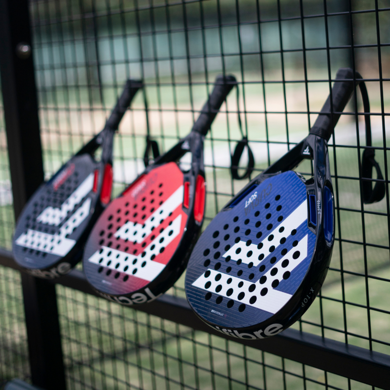 Three paddle tennis rackets hanging on a fence with a blurred background