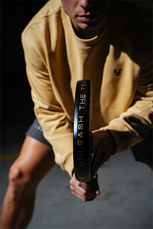 Man in a yellow jumper holding a Volt padel tennis racket. 