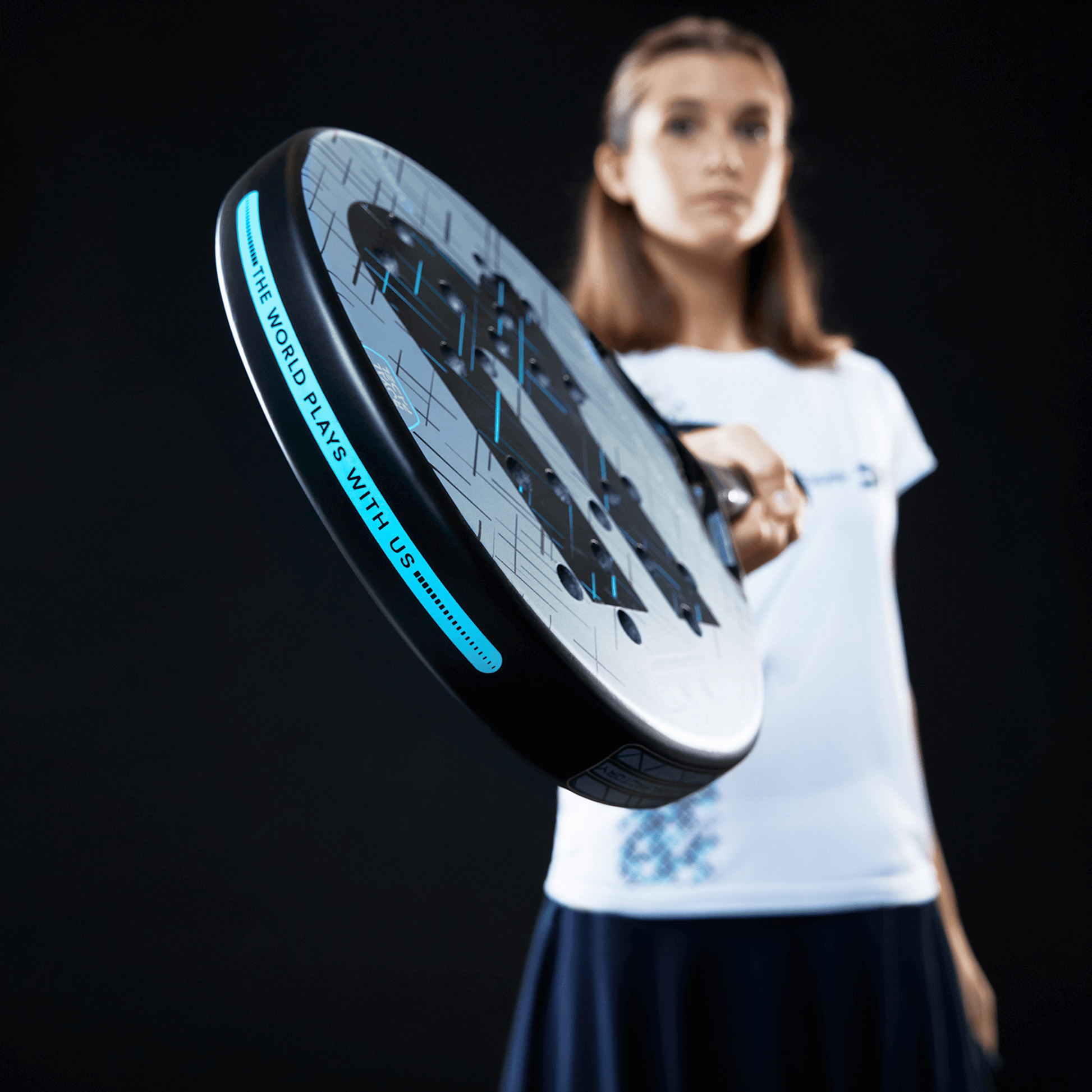 Woman holding a close-up of a blue and black Royal Padel racket with a black background