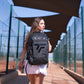 Woman walking outdoors with a black padel bag featuring a Tecnifibre logo.