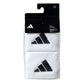 A pair of white Adidas wristbands with a black logo, in black packaging on a white background.
