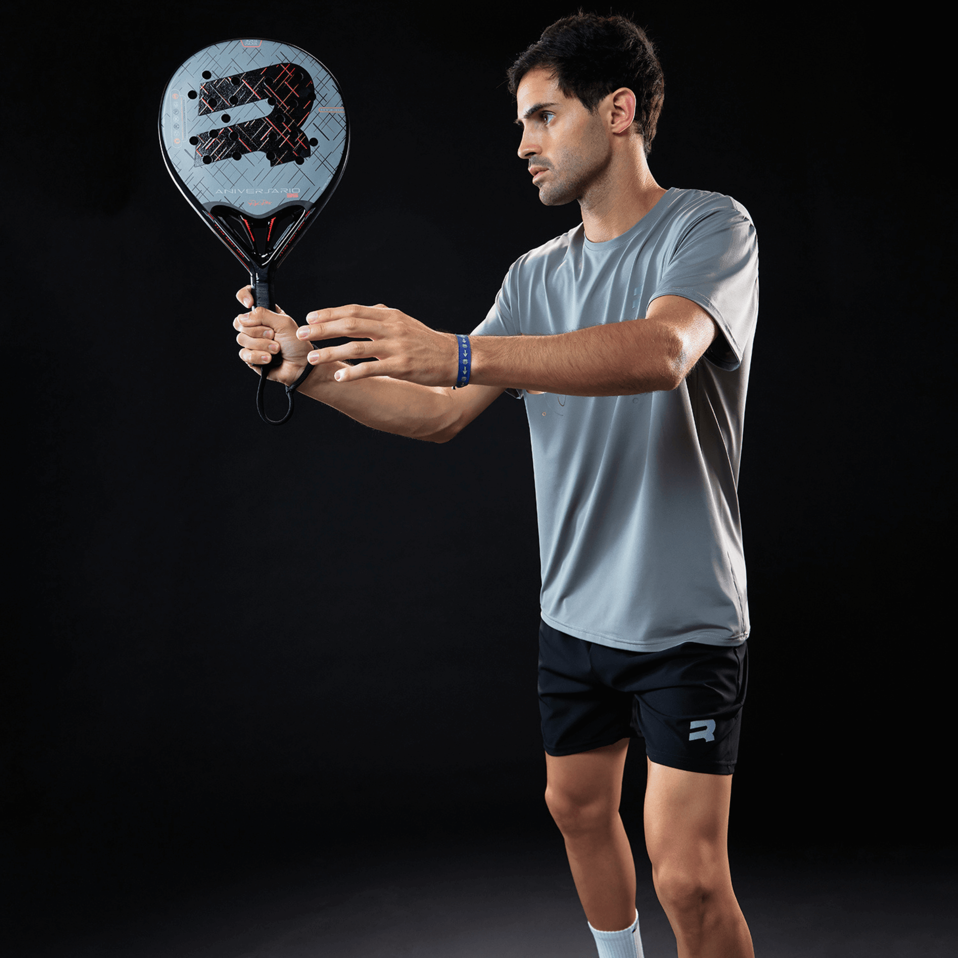 Man holding a blue padel racket with Royal Padel branding in a serve position with a black background
