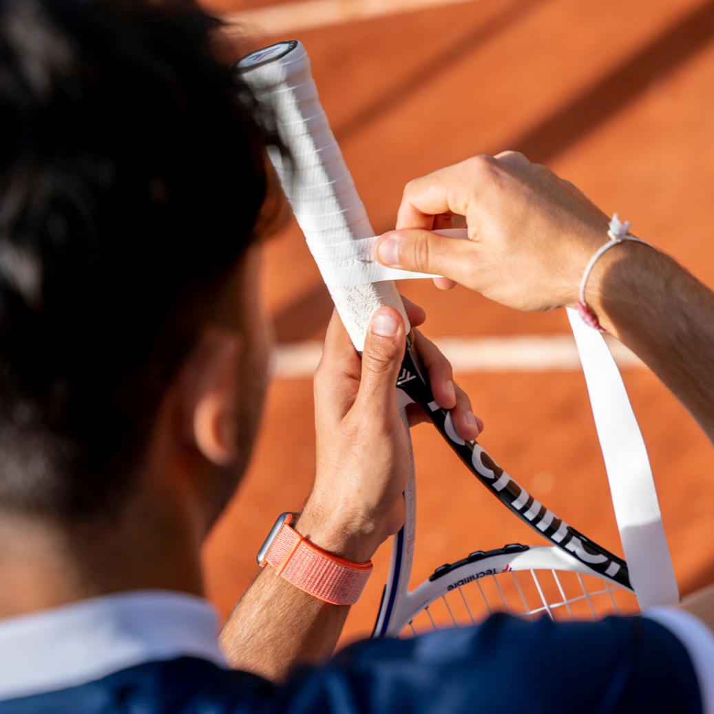 Person adjusting a tennis racket on a clay court