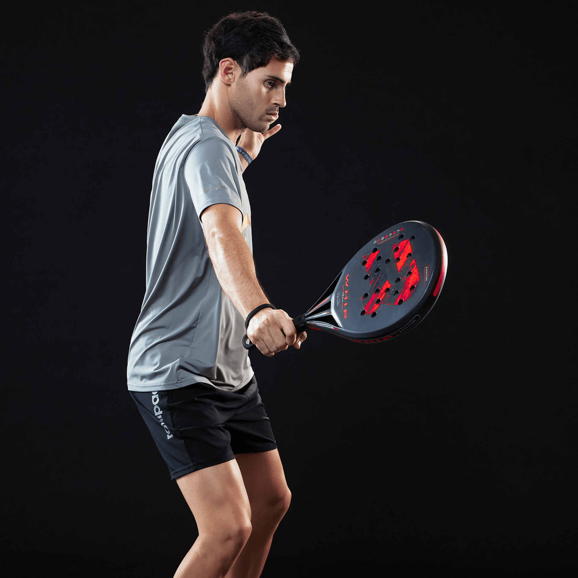 Man holding a red and black Royal Padel racket against a black background